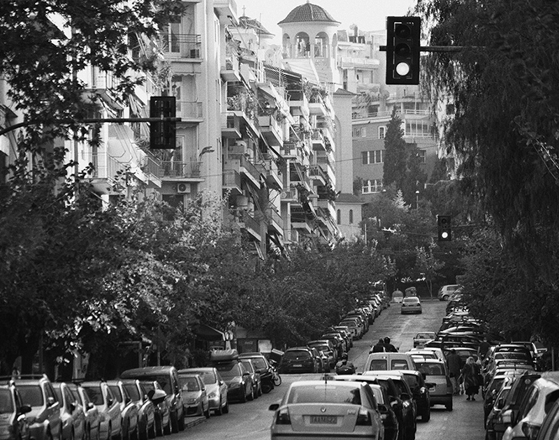 Street in Athens in black and white. Cars in traffic waiting for the traffic lights. Apartment buildings and an orthodox church in the background.